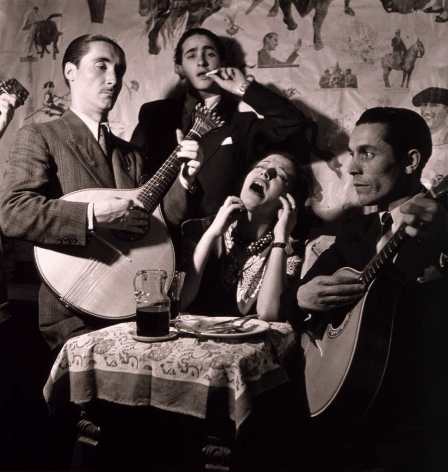 fado singer singing with two guitar players and someone smoking from behind